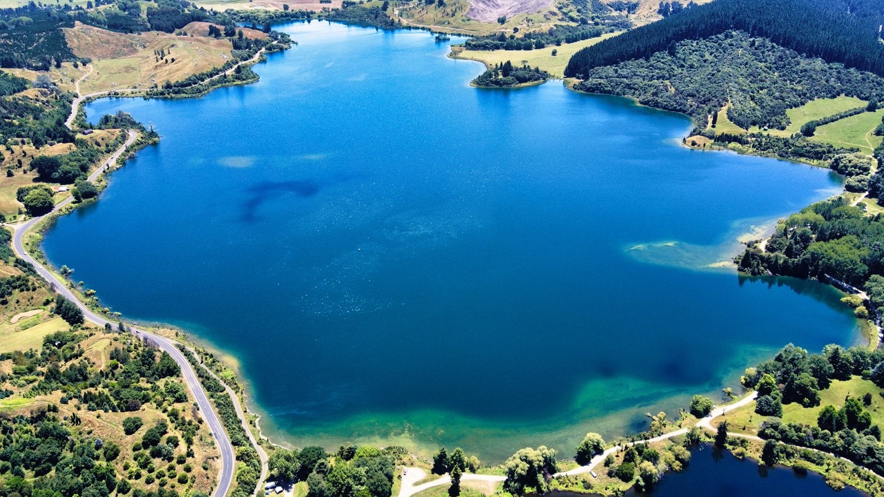 Aerial photo of Lake Tūtira in the North Island, featuring calm waters surrounded by native bush and rolling hills.