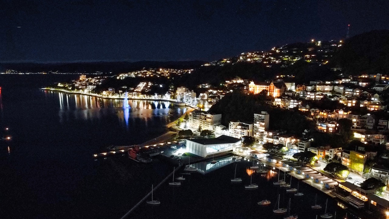 Aerial night image of Oriental Bay, Wellington, with city lights reflecting across the harbour.